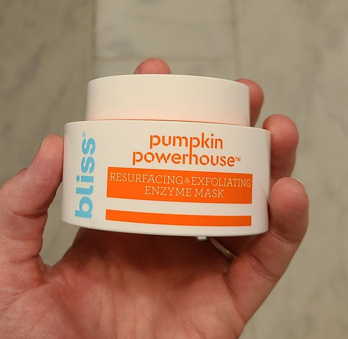 A hand holds a jar of the Bliss Pumpkin Powerhouse Resurfacing & Exfoliating Enzyme Mask.