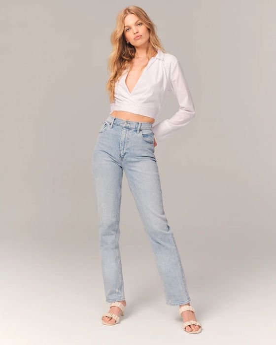 model wearing light wash jeans paired with a white deep-v long sleeve top and sandals