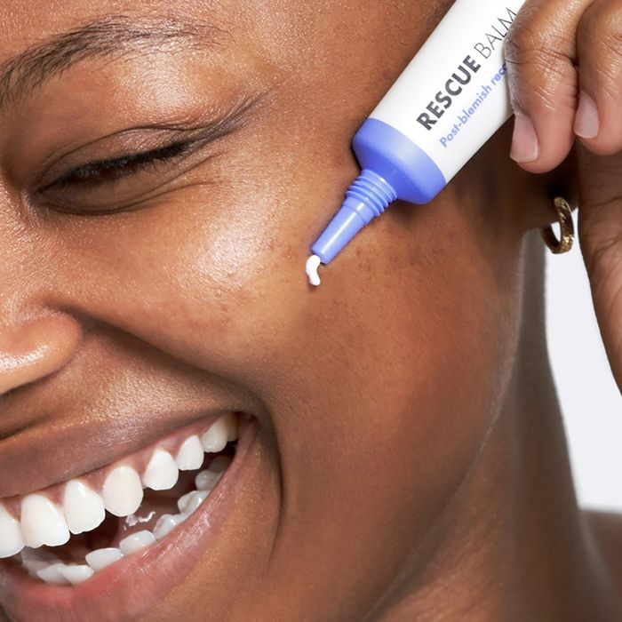 A model applying a tube of Rescue Balm to their face.