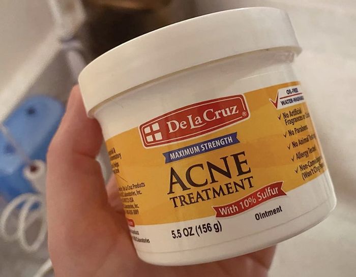 A hand holding a jar of De La Cruz acne treatment.