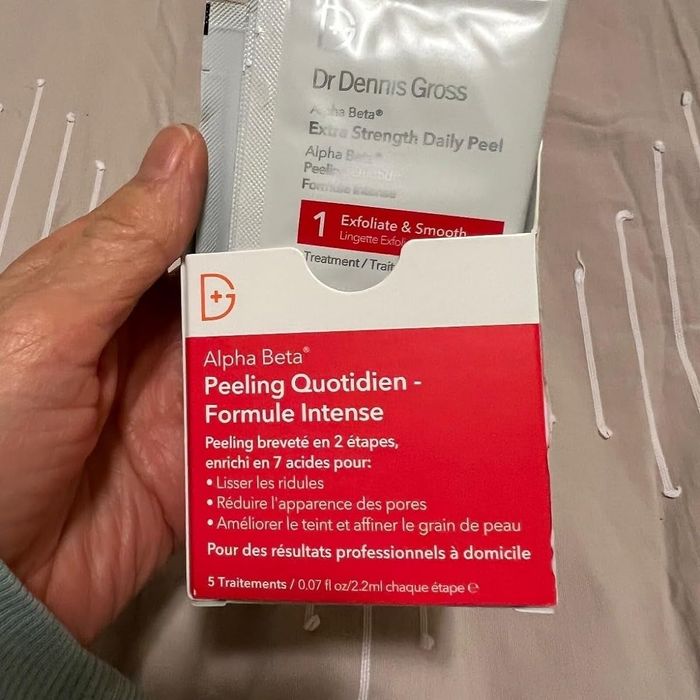 A person holding a Dr. Dennis Gross Alpha Beta Extra Strength Daily Peel packet along with instructions for clearer skin.