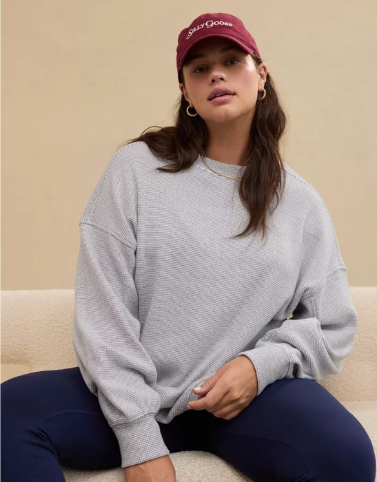 A model dressed in a casual, oversized sweater, navy leggings, and a baseball cap, posing against a neutral-colored backdrop.