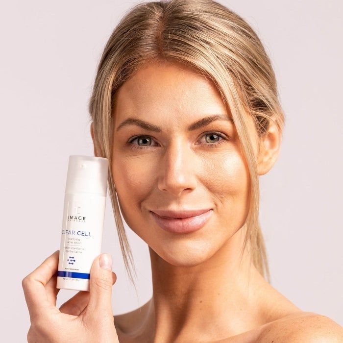 Woman holding a skincare product, looking directly at the camera, with a neutral background, ideal for shopping content