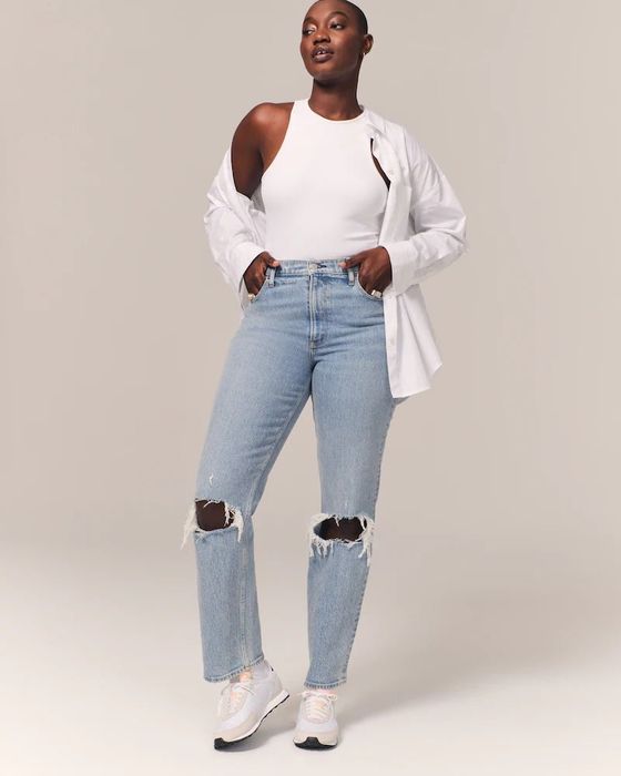 model styled in ripped light wash jeans, a white tank top, a button-down shirt, and sneakers