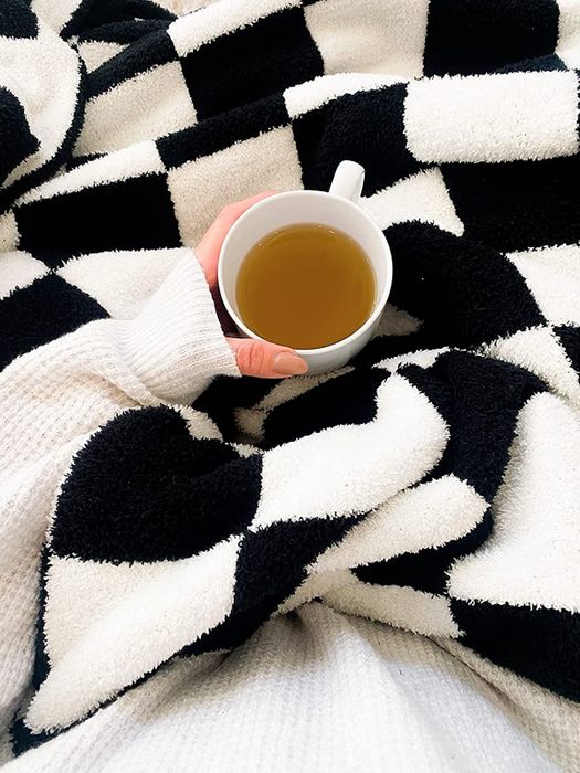 A reviewer enjoying the black and white throw blanket, wrapped up in comfort