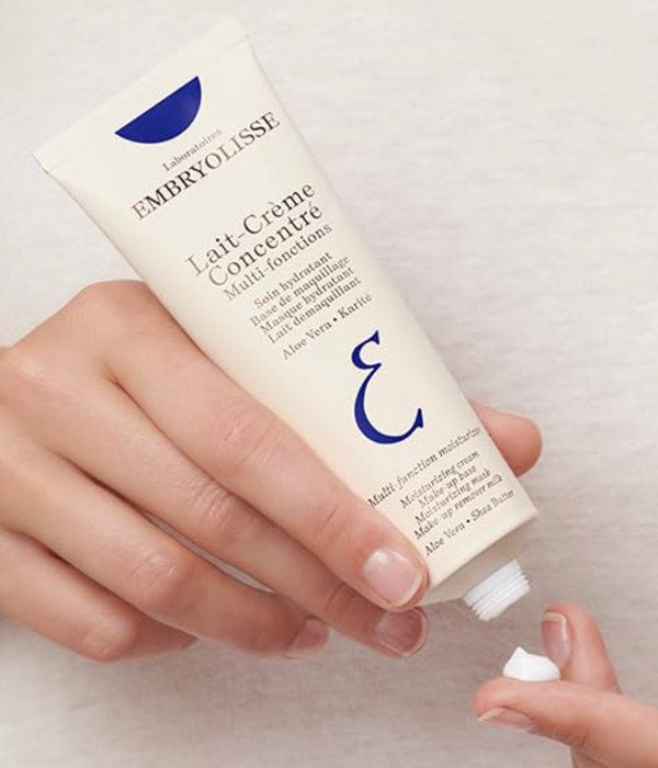 A model holding a tube of Embryolisse moisturizer with cream on their fingertip.