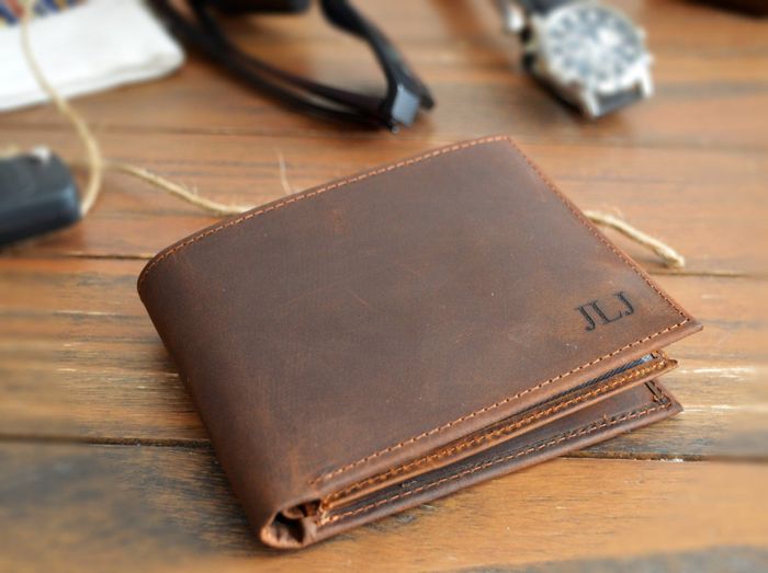 Front view of a brown leather wallet with initials engraved in the lower right corner