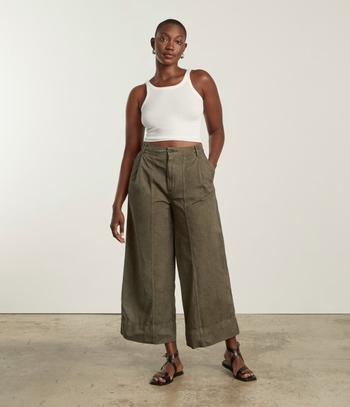 model styled in olive green wide-leg pants, a white tank top, and black sandals