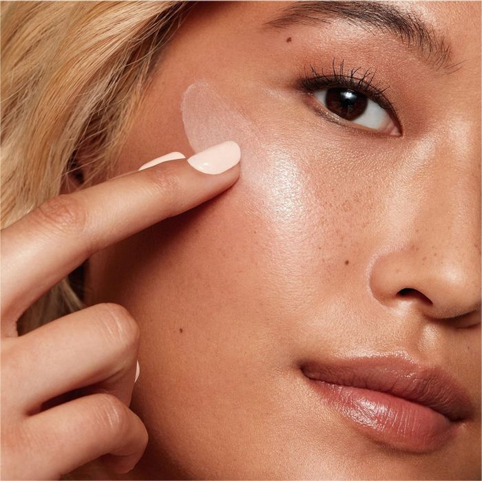 A close-up of a person gently applying moisturizer to their cheek.