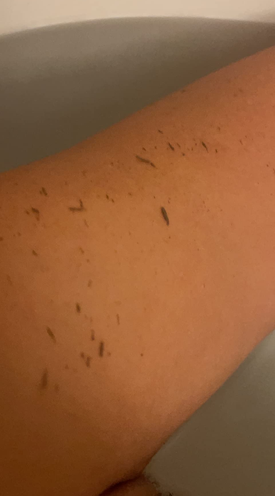 A close-up shot of a person's arm submerged in a bathtub filled with water, with visible dirt or small particles on their skin