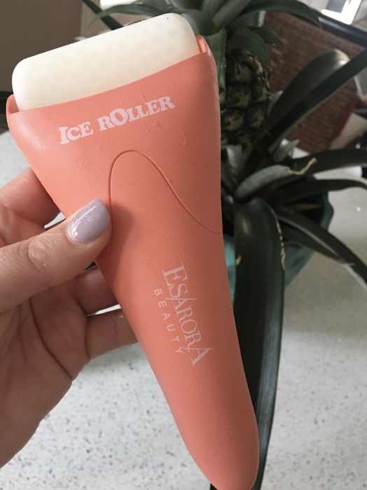 A reviewer's hand holding an ice roller that resembles a shaving razor, with a rolling bar at its end for smooth application.