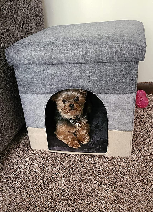 A small dog comfortably resting inside the gray ottoman.