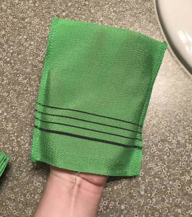 A photo of a reviewer proudly holding up the green exfoliating towel