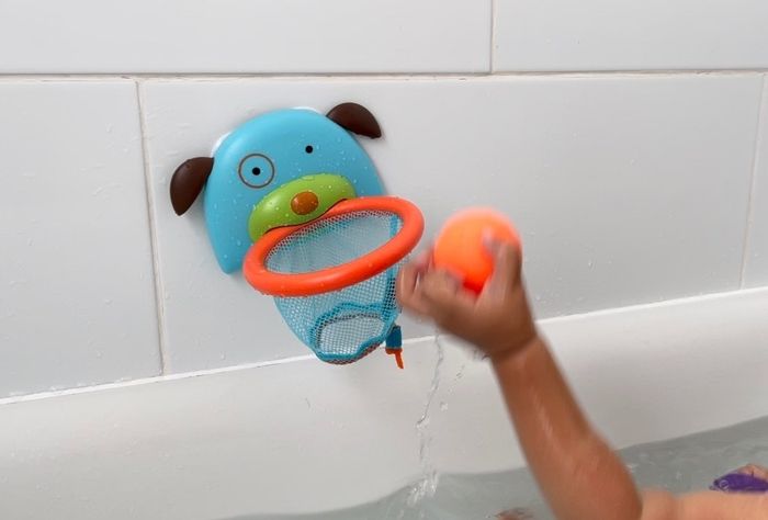 A bath-time basketball toy mounted on a tiled wall, with a child preparing to shoot the ball into the hoop.