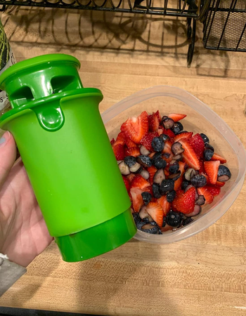 A reviewer shows off the green cylindrical cutter, holding it next to a container of freshly cut fruit, ready for snacking.