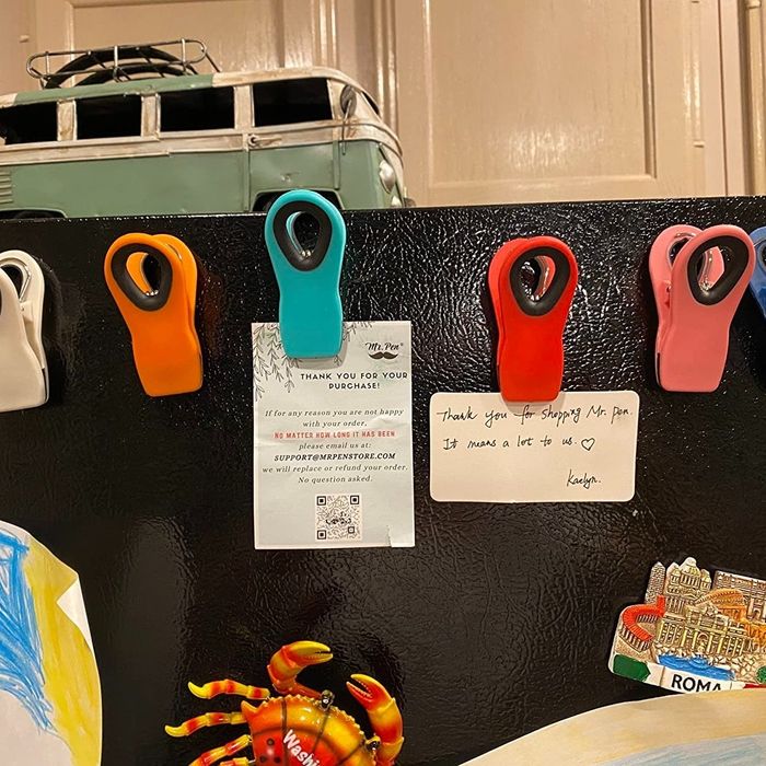 A refrigerator door is adorned with vibrant clips, holding notes and drawings. One of the notes reads, 'Thank you for shopping.'