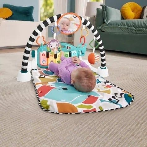 A baby lies on a vibrant play mat, surrounded by various hanging toys beneath an activity gym in a cozy living room. A round mirror reflects the baby's smiling face.