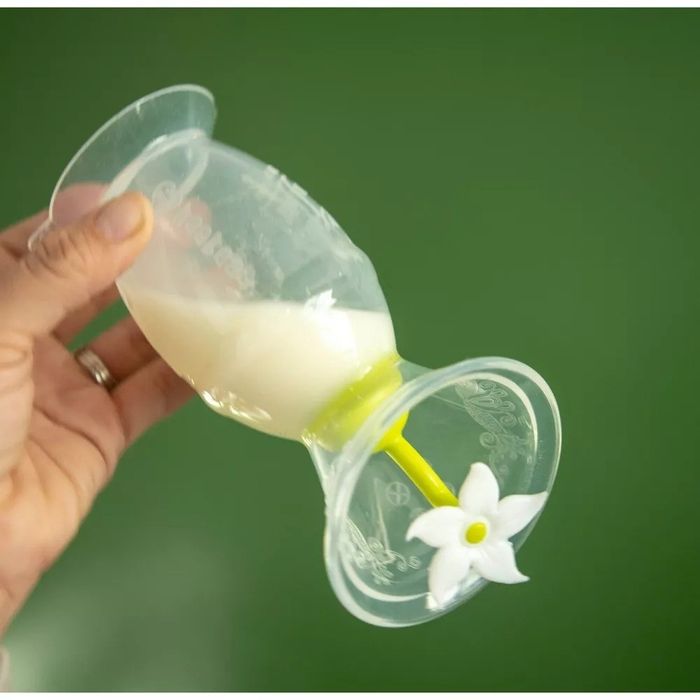 A hand holding a breast pump with milk inside