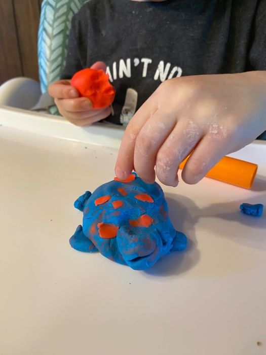 A child uses a blue turtle-shaped mold with Play-Doh, holding an orange tool and a piece of red Play-Doh in their hands.