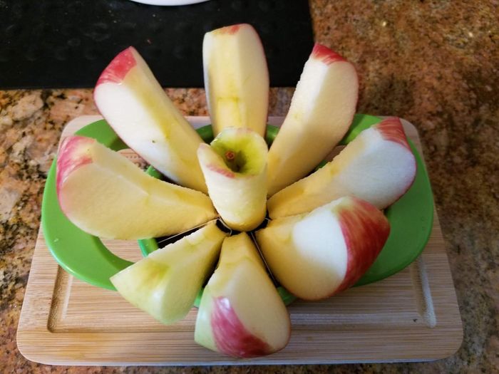 A reviewer captured a photo of a sliced red apple, neatly divided using a green apple slicer, and placed it on a rustic wooden cutting board, showcasing its fresh, juicy appeal.