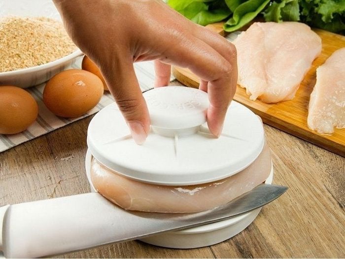 A two-piece kitchen slicer with a model's hand gripping the top handle, effortlessly slicing through a chicken breast.