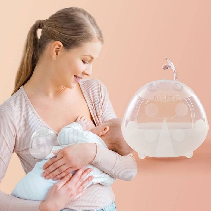 A person is using a silicone manual breast pump while holding their baby