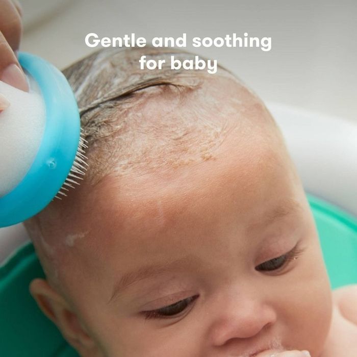 A close-up shot of a baby having their hair gently washed using a soft brush. The caption reads: