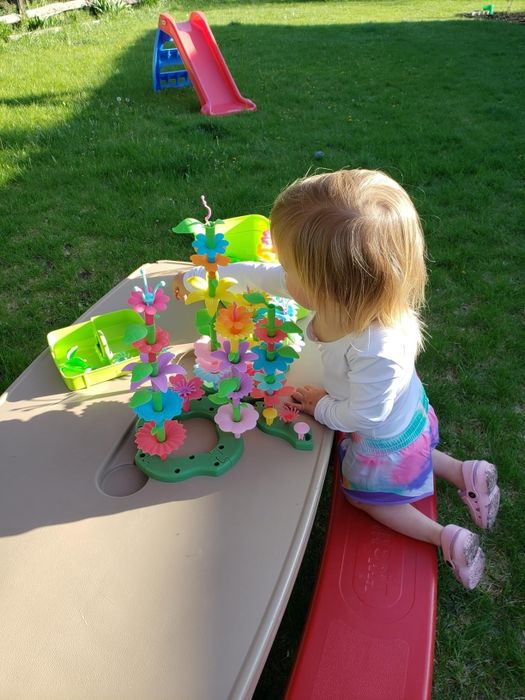 A toddler enjoys playing with a vibrant flower-building toy at an outdoor water table.