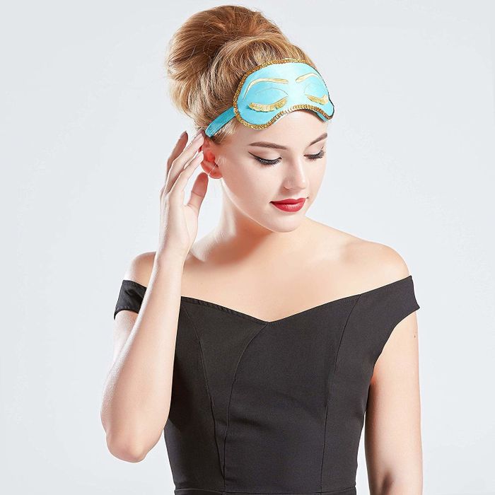 A model wearing the blue eye mask, featuring gold trim, embroidered closed eyes, and fringed lashes.