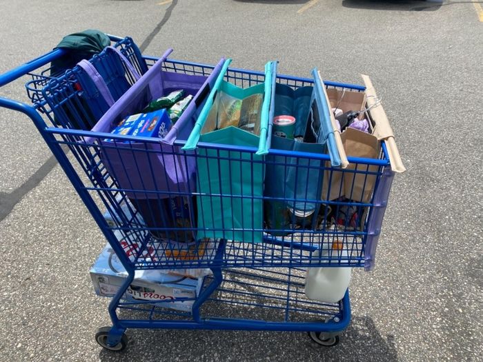 A shopping cart filled with reusable bags, brimming with groceries, and a case of water resting on the lower shelf.