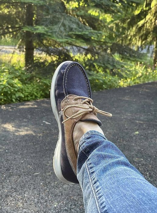 Close-up of a person wearing blue jeans and casual boat shoes while lounging outdoors, highlighting the comfort of the footwear in a natural setting.