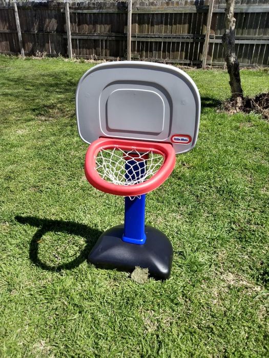 A child's basketball hoop with a red rim and blue stand, placed on a grassy lawn
