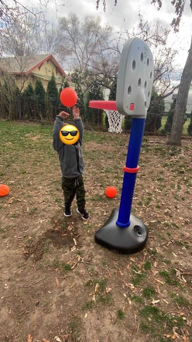 A child enjoying a game of basketball with a toy hoop in the backyard