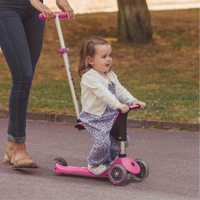 A young child sitting on the scooter, being pushed by an adult