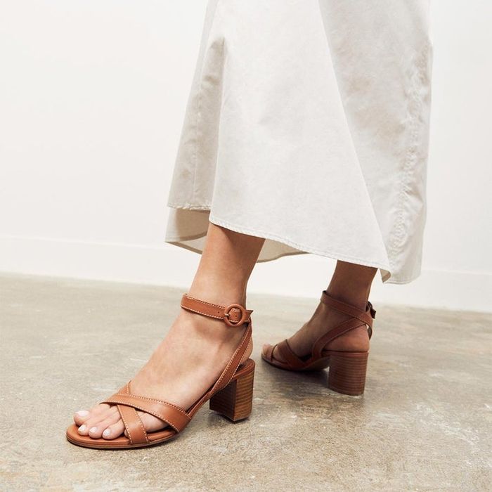 A person wearing a white skirt and brown strappy block-heeled sandals, adding a touch of elegance to their outfit.