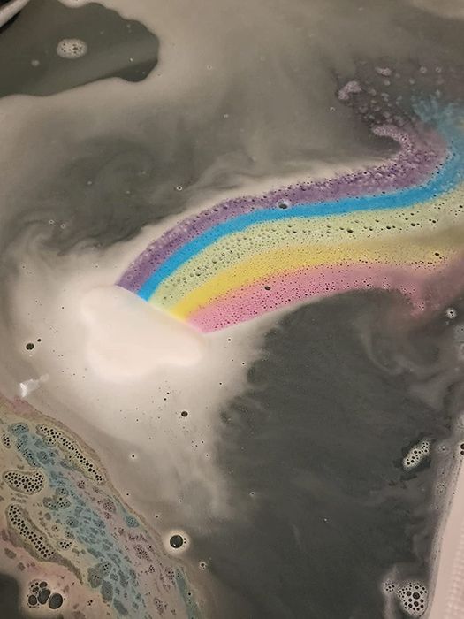 The cloud-shaped bath bomb dissolving in a tub, creating a mesmerizing rainbow effect.