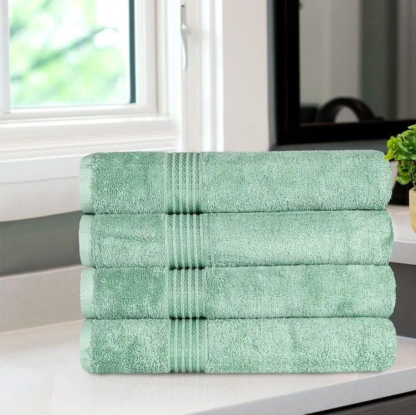 A neat stack of four folded green towels, arranged one on top of the other.