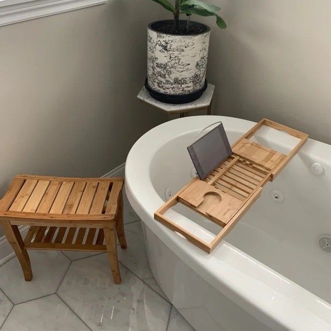 A tray placed on a bathtub, complete with a glass of wine and a book.