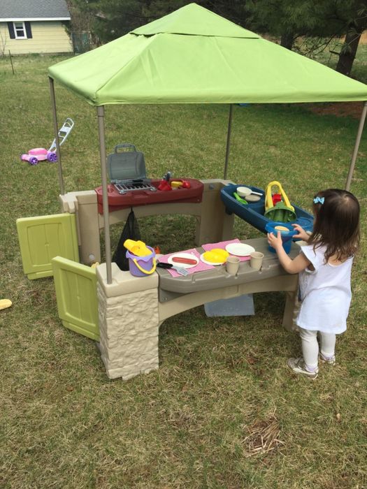 A child playing with a toy kitchen set under a canopy in a backyard