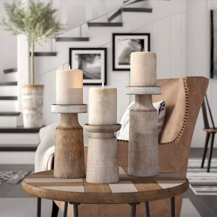 Three wooden candle holders with candles resting on an end table.