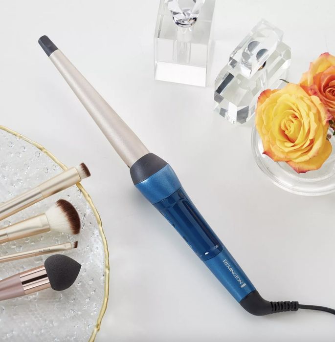 A blue and black curling wand, makeup brushes, and a yellow rose