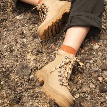 A person seated on rocky terrain, wearing beige hiking boots and dark pants.