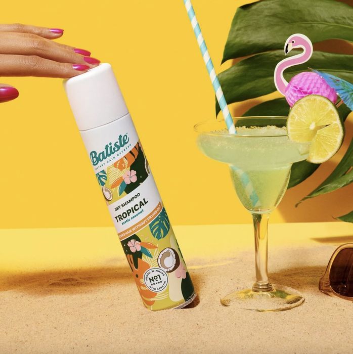 A can of dry shampoo, a margarita glass, and a person with a pink manicure