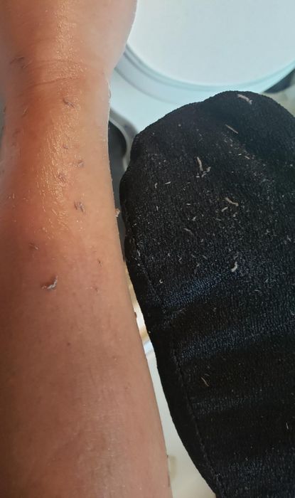 A detailed view of a black glove alongside a reviewer's leg, showcasing flakes of dull gray skin.