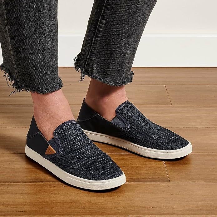 A pair of slip-on casual shoes modeled with frayed hem jeans on a wooden floor, creating a relaxed and stylish look.