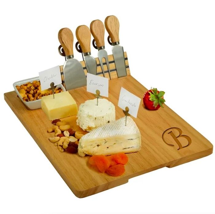 A wooden board featuring cheese knives, cheese, fruit, and nuts.