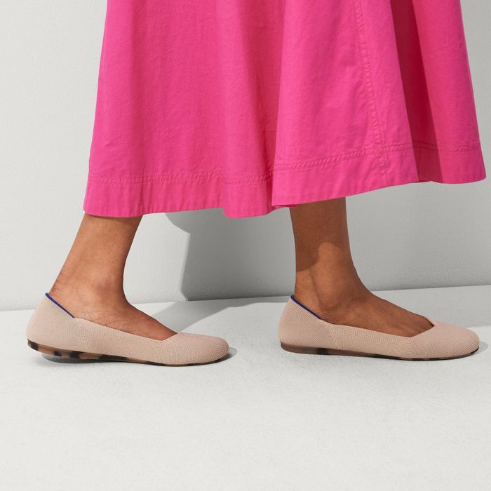 A close-up image of a person wearing a pink skirt paired with beige ballet flats.
