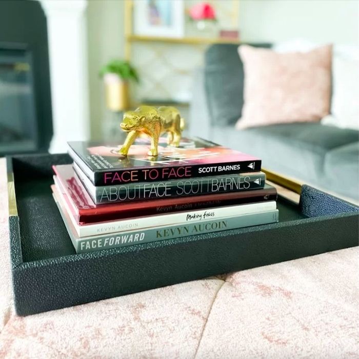 A photo of a tray on a coffee table, holding a stack of books and a stylish gold accessory.