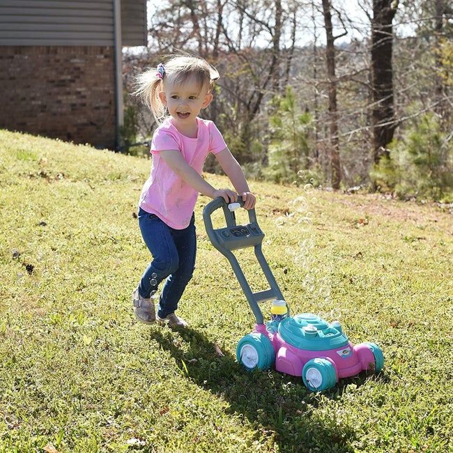 A child pushing a pink and teal blue lawn mower with bubbles floating around it