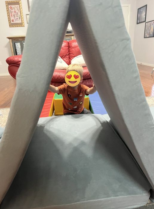 A toddler enjoying playtime in a soft, foldable playhouse structure indoors, surrounded by vibrant toys